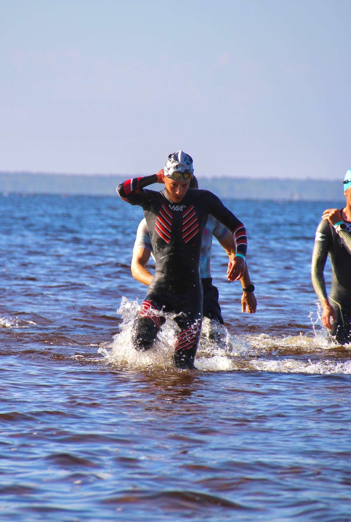 Elian Gaborit sort de l'eau en courant, en combinaison de triathlon, bonnet et lunettes de natation, au milieu d'autres concurrents.